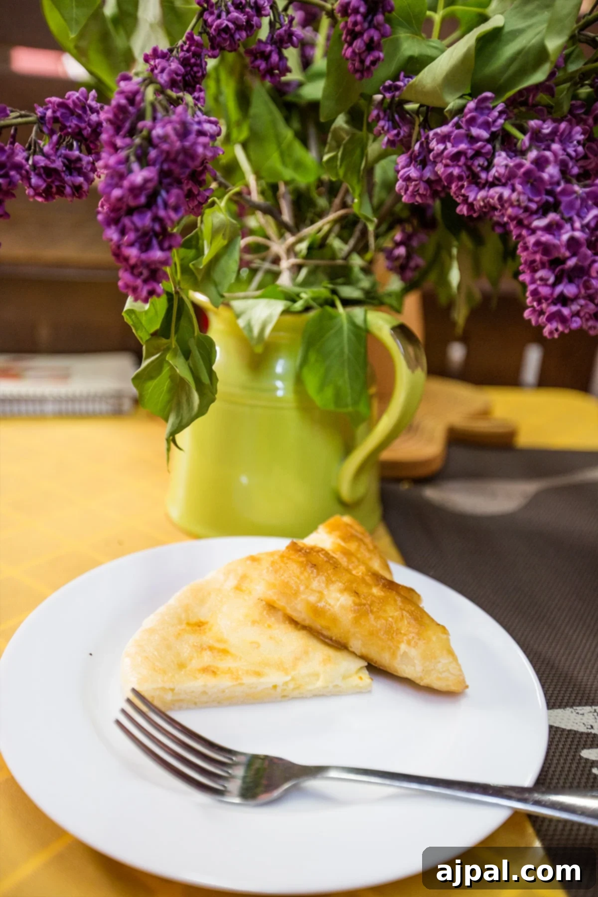 A plate of Khachapuri, Georgian cheese bread, with lilac flowers in the background at a cozy Tbilisi cafe.