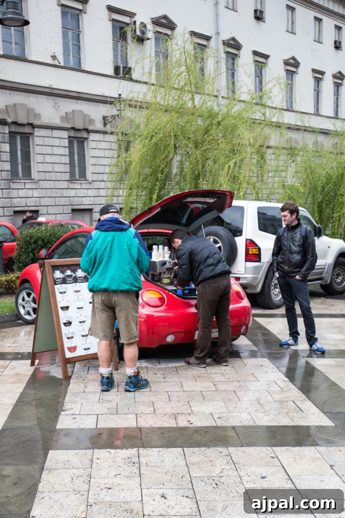 People getting espresso from a mobile coffee shop operating from the back of a red Volkswagen Beetle in Tbilisi, offering coffee to go.