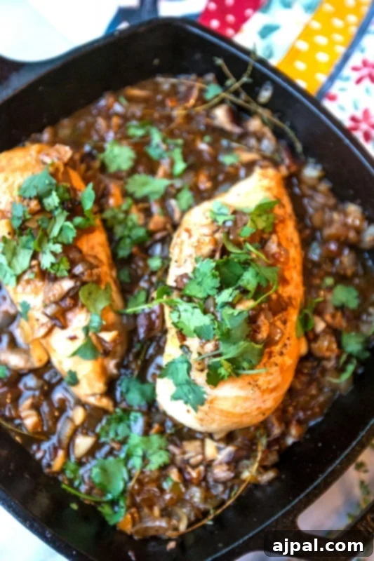 Close-up of skillet chicken with a rich, glossy mushroom and onion sauce, topped with fresh herbs.