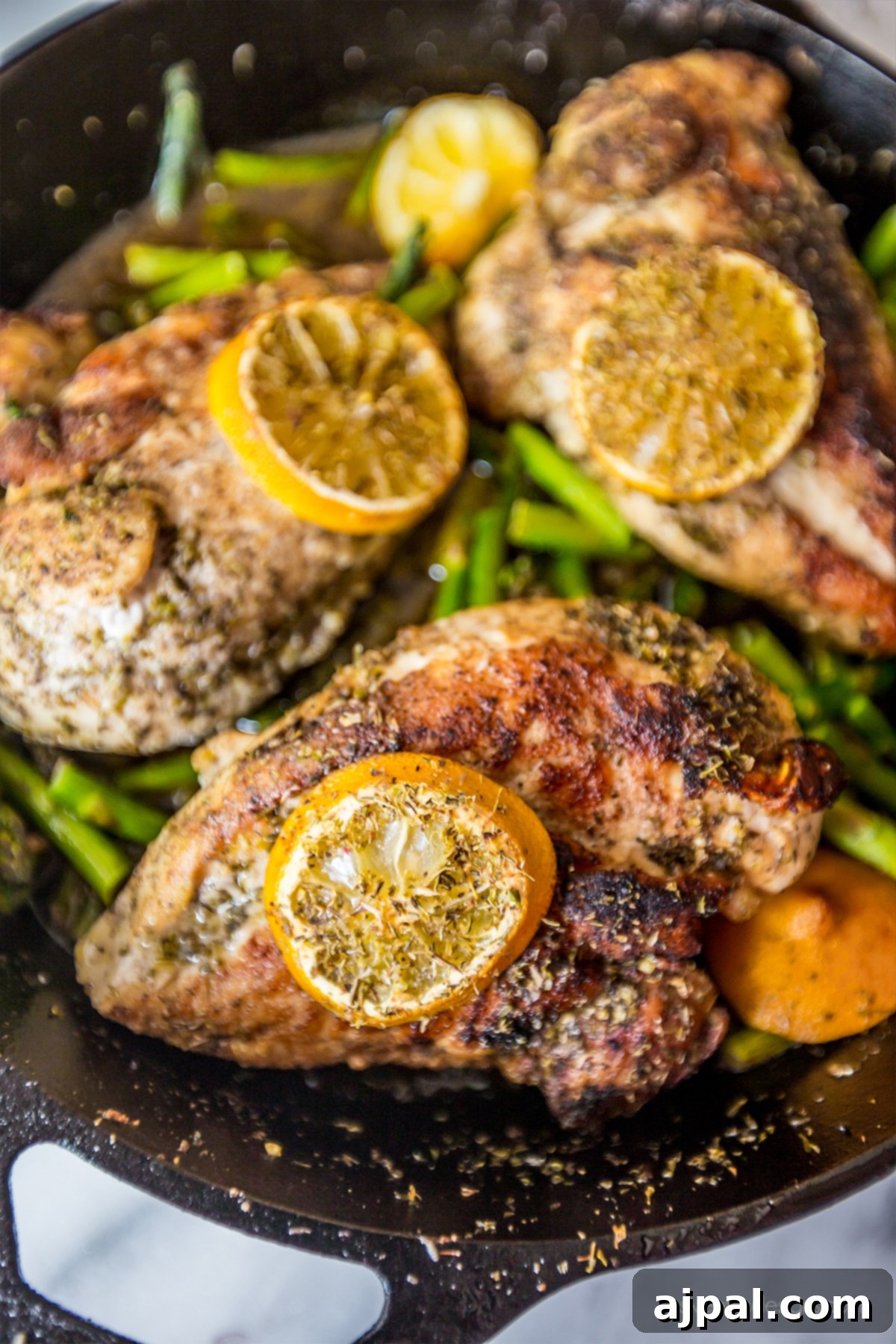 Cast iron skillet featuring golden-brown lemon chicken and tender asparagus spears, garnished with fresh lemon slices, ready to serve.