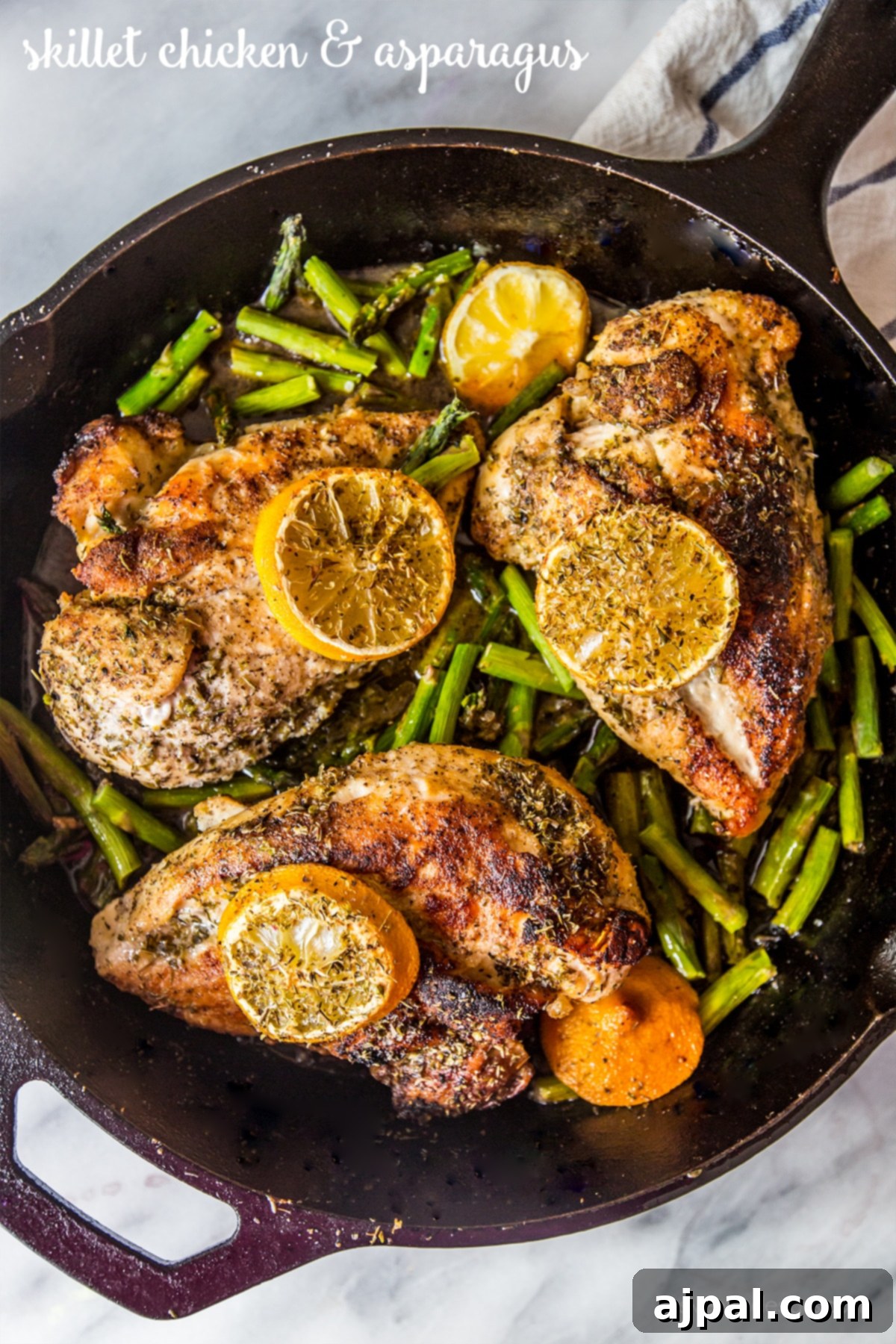 Close-up of a cast iron skillet filled with beautifully seared chicken, bright green asparagus, and thin lemon slices, showcasing a delicious one-pot meal.