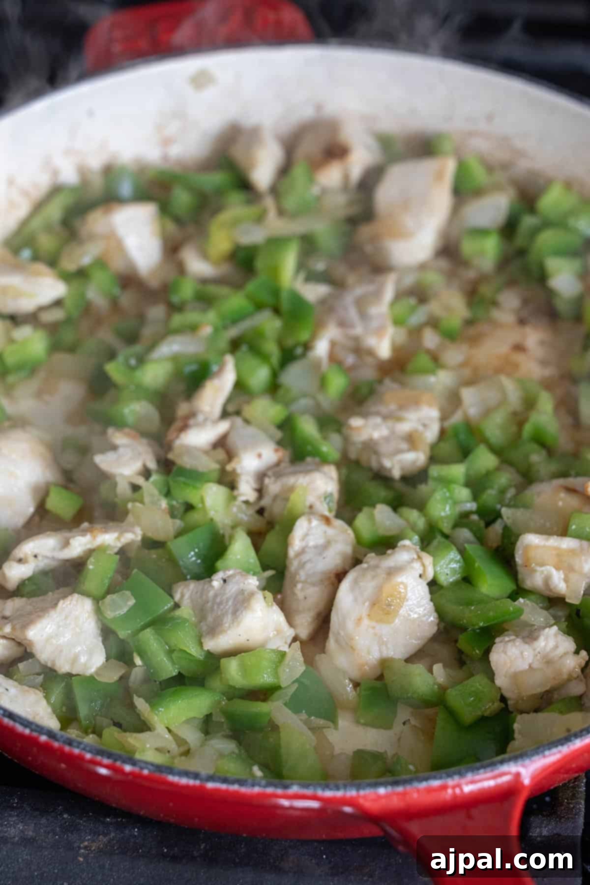 A red skillet contains a mixture of chopped green bell peppers, diced onions, and pieces of chicken cooking together, perfect for starting an easy risotto recipe.