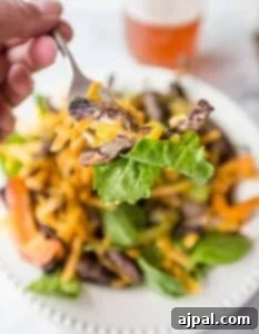 Sizzling Fajita Steak Salad 4 A person is eating a steak salad with a fork.