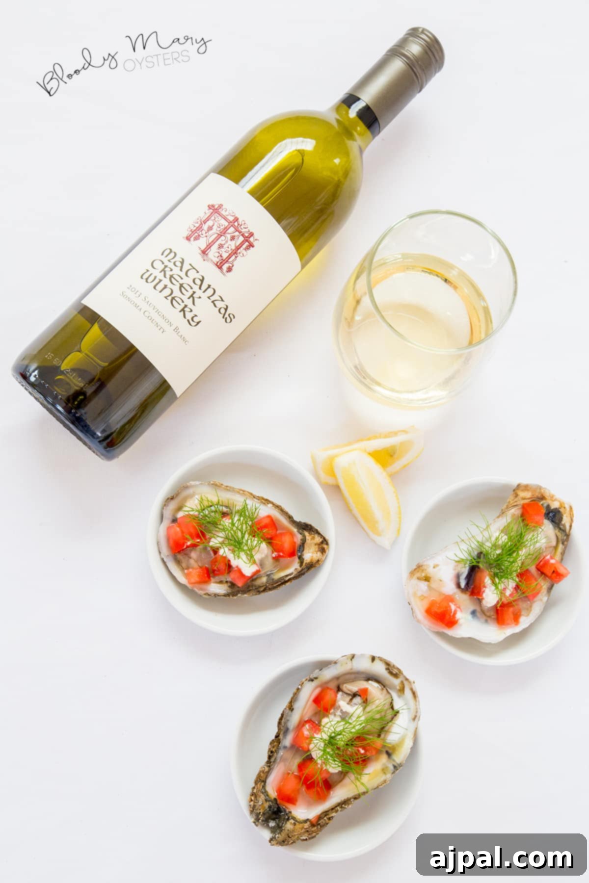 Freshly shucked oysters topped with diced tomatoes and dill, served alongside a bottle and glass of white wine.