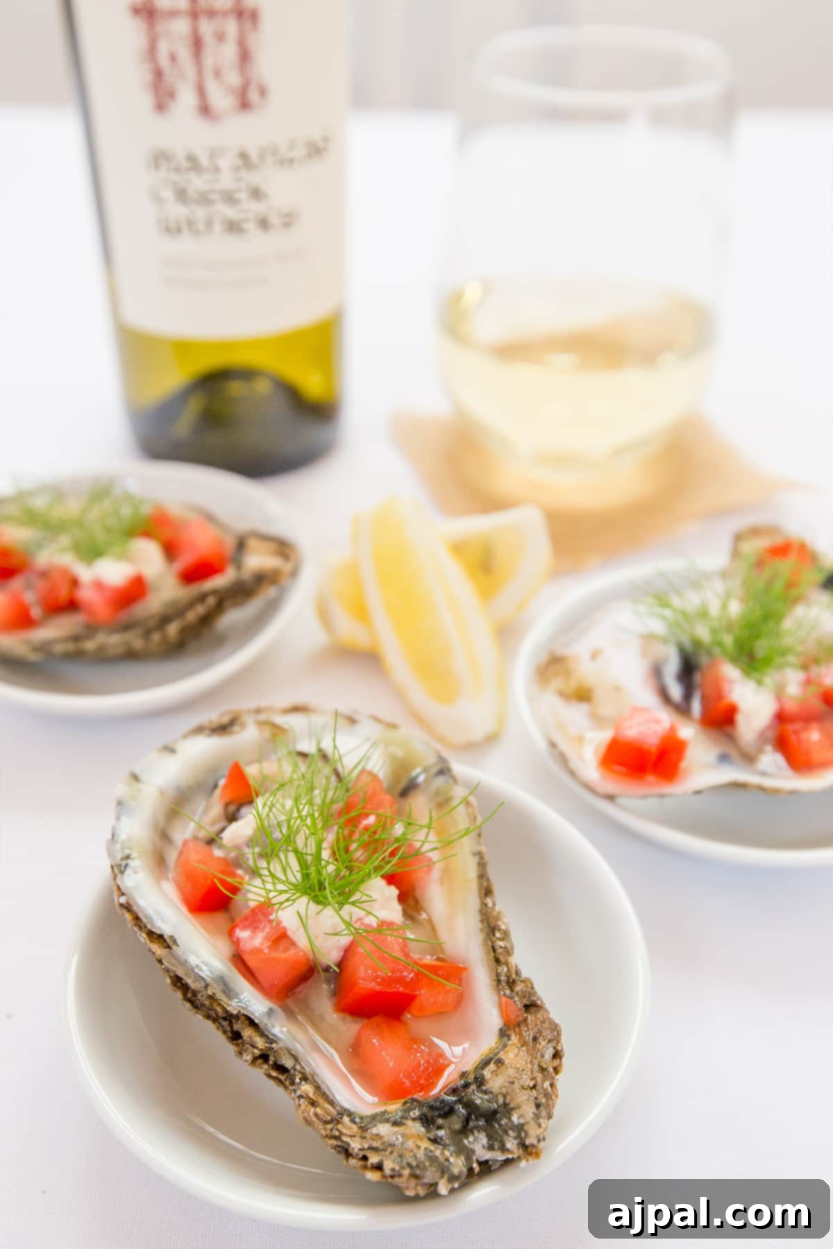 Close-up of Bloody Mary Oysters garnished with fresh dill on a plate, with a bottle of white wine blurred in the background.