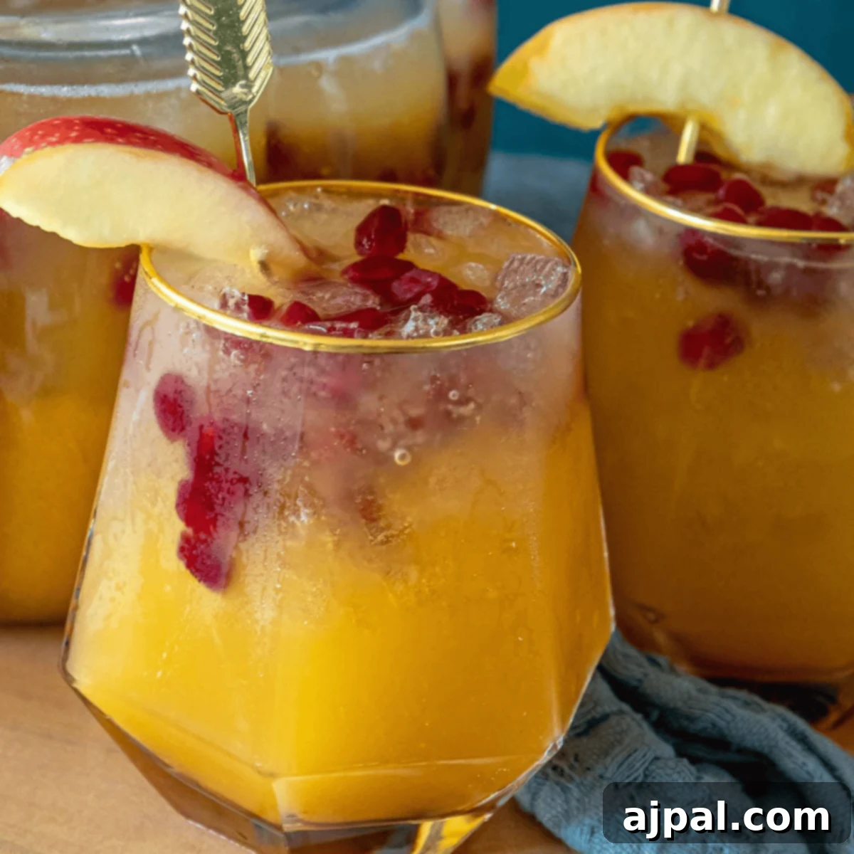 Spooktacular Halloween Treats You Need to Try 20 Two glasses filled with a yellow-orange pumpkin punch cocktail, garnished with red pomegranate seeds and apple slices, with a pitcher of the same festive drink in the background.