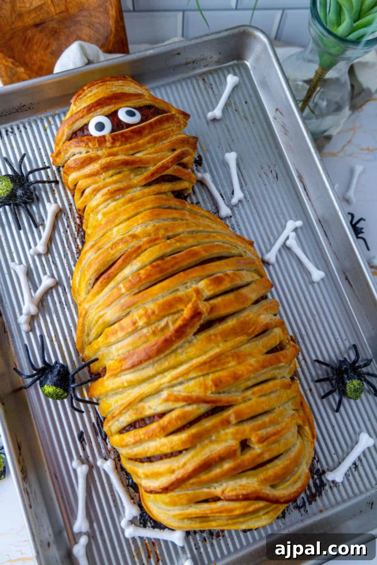 Spooktacular Halloween Treats You Need to Try 22 A tray features a mummy-shaped meatloaf with googly eyes, surrounded by decorative bones and spiders.