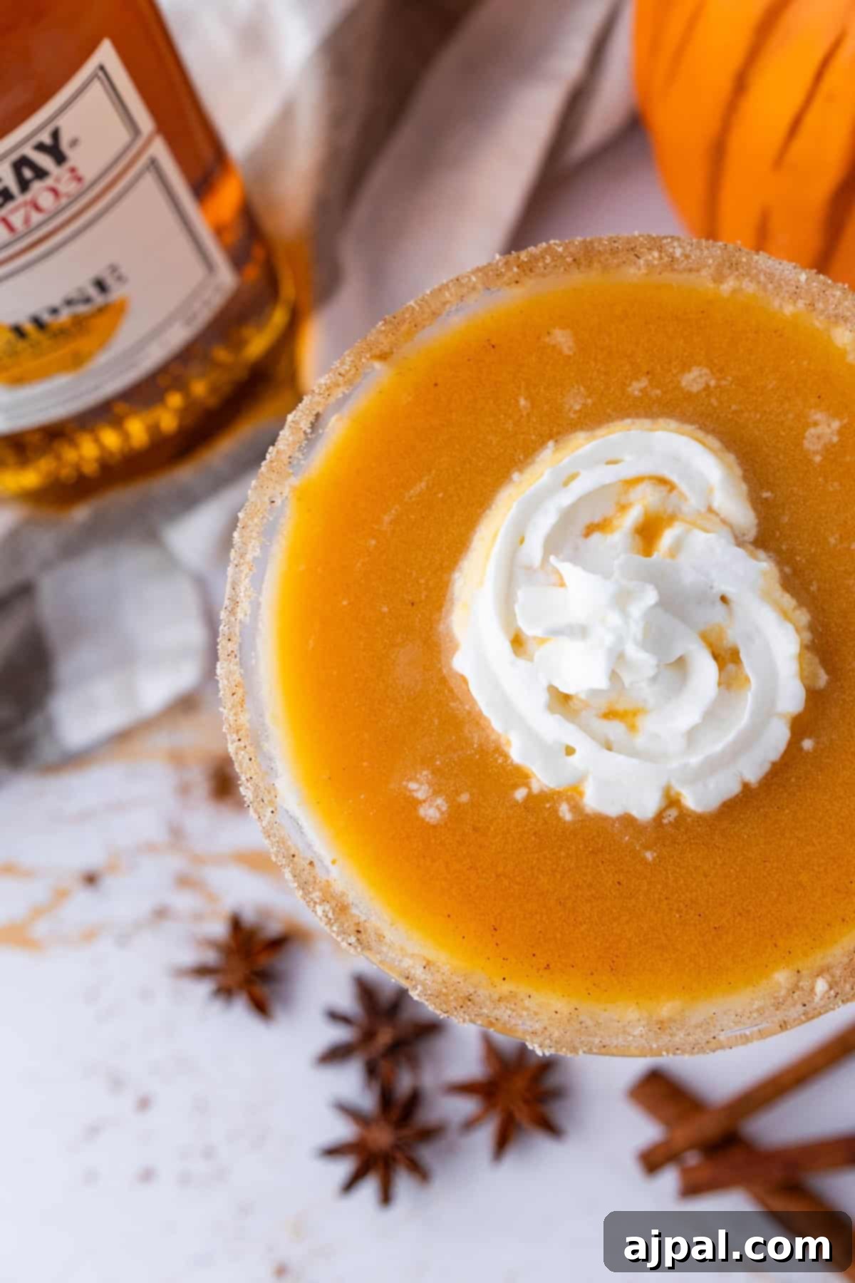 Spooktacular Halloween Treats You Need to Try 33 A close-up of a pumpkin pie martini topped with whipped cream. Star anise and cinnamon sticks are scattered on the table. A bottle of whiskey is partially visible in the background.