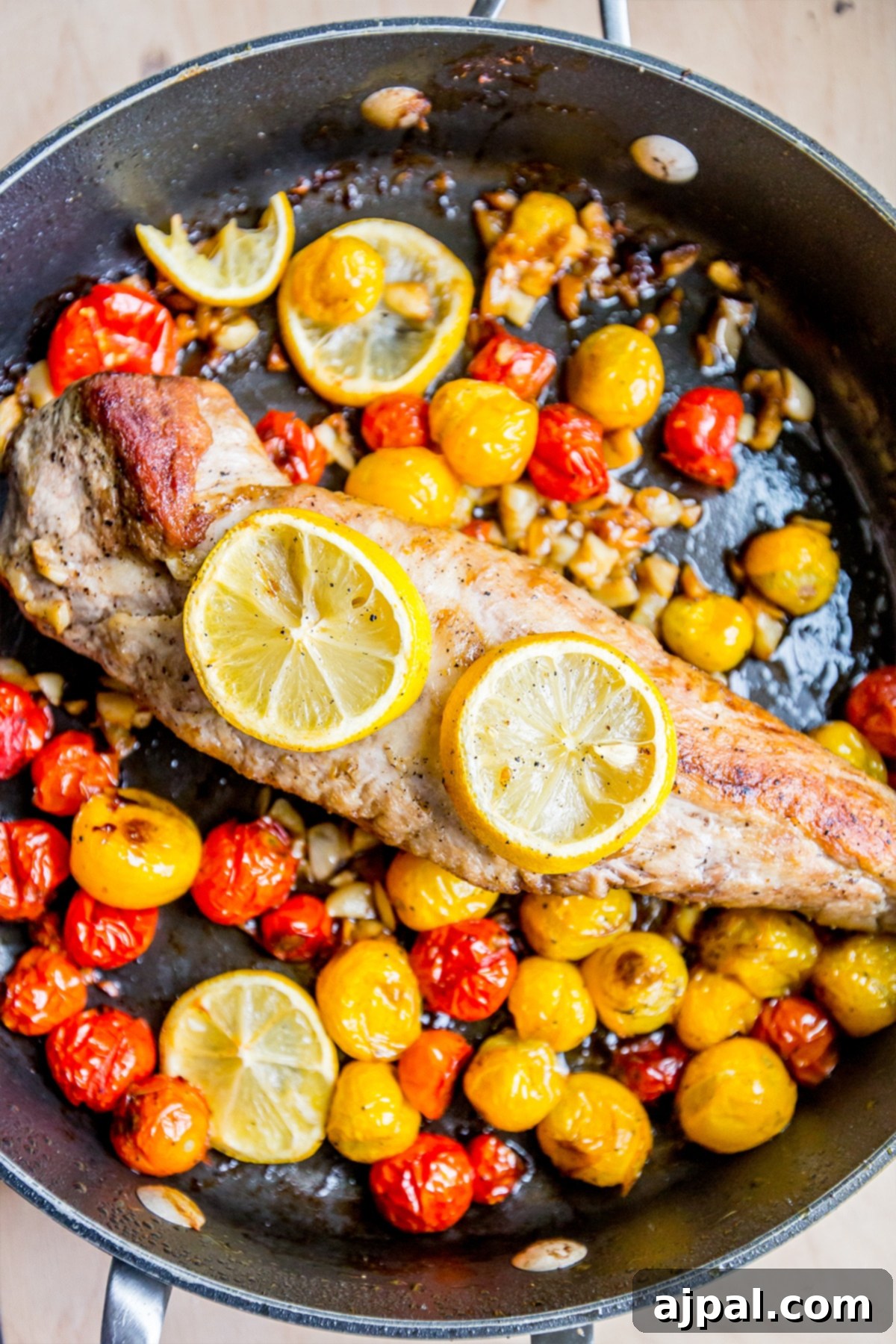 Five-Ingredient Tuscan Pork Loin Skillet Dinner 2 Pan with pork tenderloin, lemons, garlic, and tomatoes around it, cooked to perfection.
