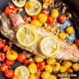 Effortless One-Pan Tuscan Pork Loin (5 Ingredients) 6 A cooked piece of One Pan Tuscan Pork Loin garnished with lemon slices surrounded by yellow and red cherry tomatoes in a pan.