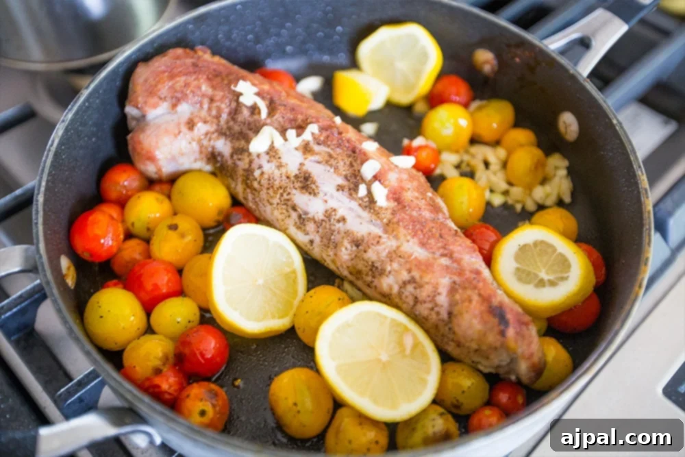 Effortless One-Pan Tuscan Pork Loin (5 Ingredients) 3 A succulent pork tenderloin browning beautifully in a skillet on the stove, surrounded by bright lemon slices and ripe cherry tomatoes.