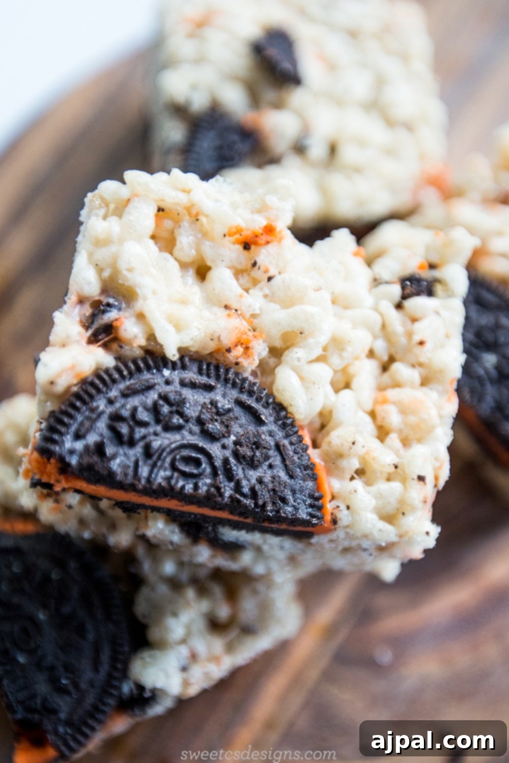 Close-up of Halloween Oreo Krispie Treats, showcasing the crushed Oreos within the rice krispie mixture, on a wooden cutting board.