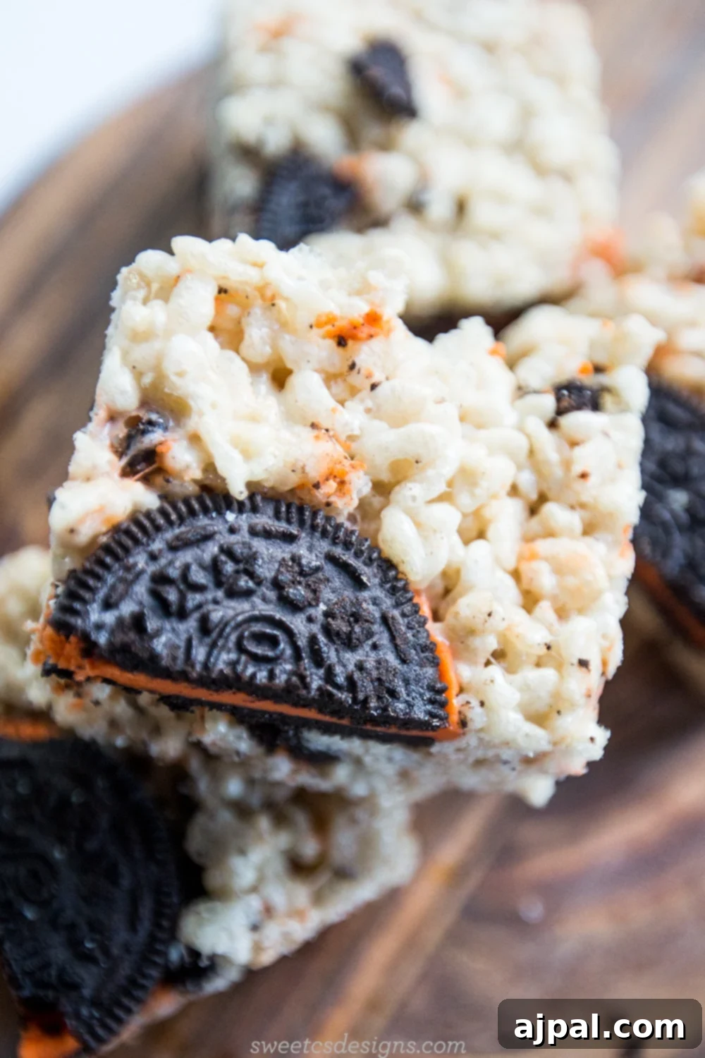 Close-up of Halloween-themed Oreo Krispie Treats with visible orange creme and chocolate cookie pieces, arranged artfully on a wooden cutting board.