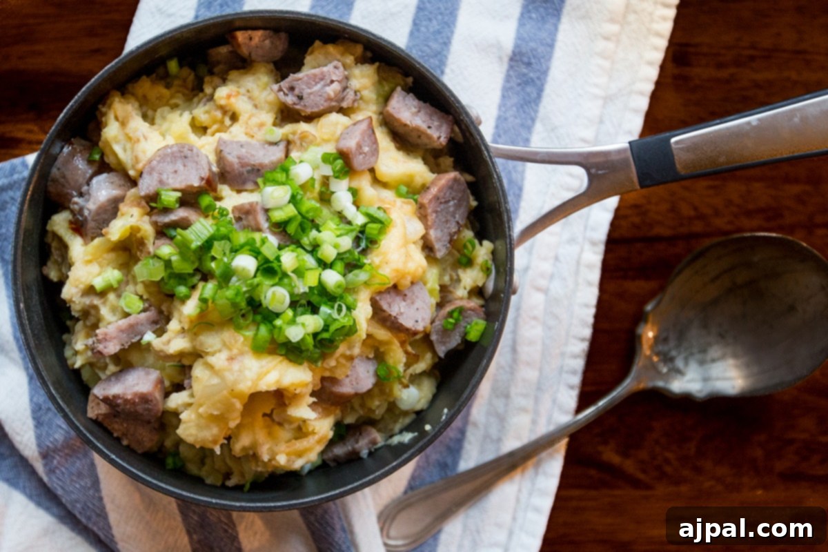 Hearty Cheesy Sausage Potato and Cabbage Bake 5 A close-up of cheesy sausage colcannon in a skillet, adorned with fresh green onions.