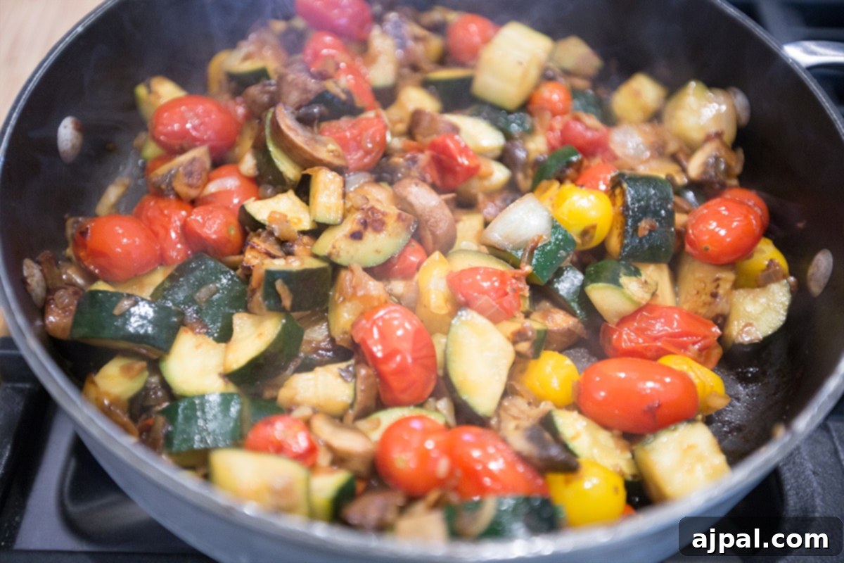 A large pan filled with sautéed mushrooms, zucchini, onion, and cherry tomatoes, perfectly cooked and fragrant.