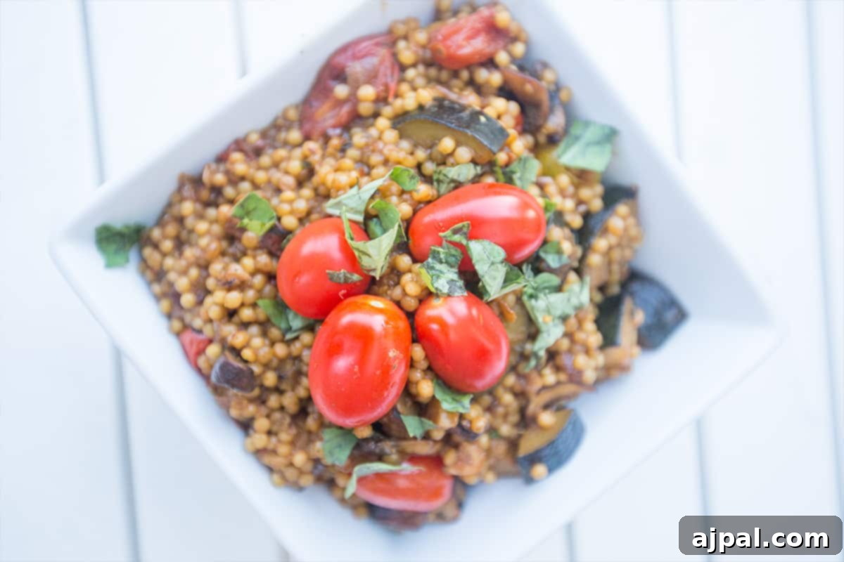 A close-up of a serving of flavorful couscous loaded with sautéed onions, mushrooms, zucchini, tomatoes, and fresh basil.