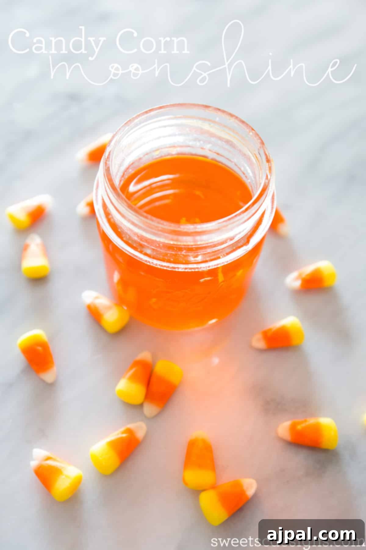 Candy Corn Elixir 2 A glass jar filled with vibrant orange candy corn moonshine, surrounded by scattered candy corn pieces.