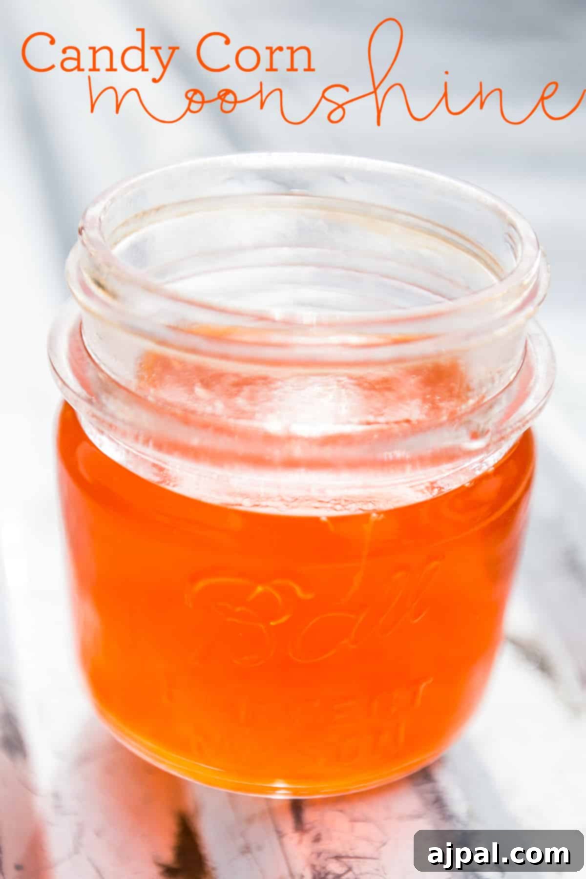 Candy Corn Elixir 3 A clear jar of vibrant orange candy corn infused moonshine, ready for festive Halloween celebrations.
