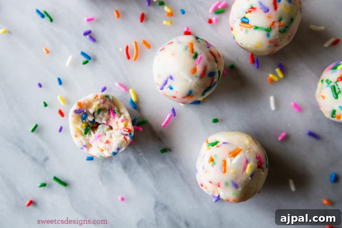 Close-up of delectable cake batter truffles, generously coated with colorful sprinkles, resting on a pristine marble countertop. A truly yum, two-ingredient dessert!