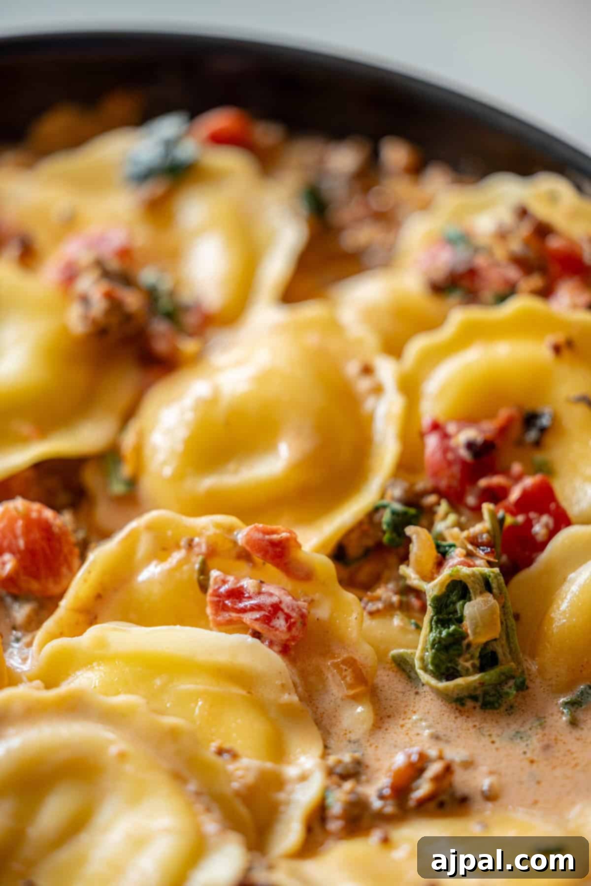 Creamy Tuscan Sausage Ravioli 2 Close-up of creamy ravioli with sausage, featuring chopped tomatoes, fresh spinach, and aromatic herbs in a rich Tuscan cream sauce.