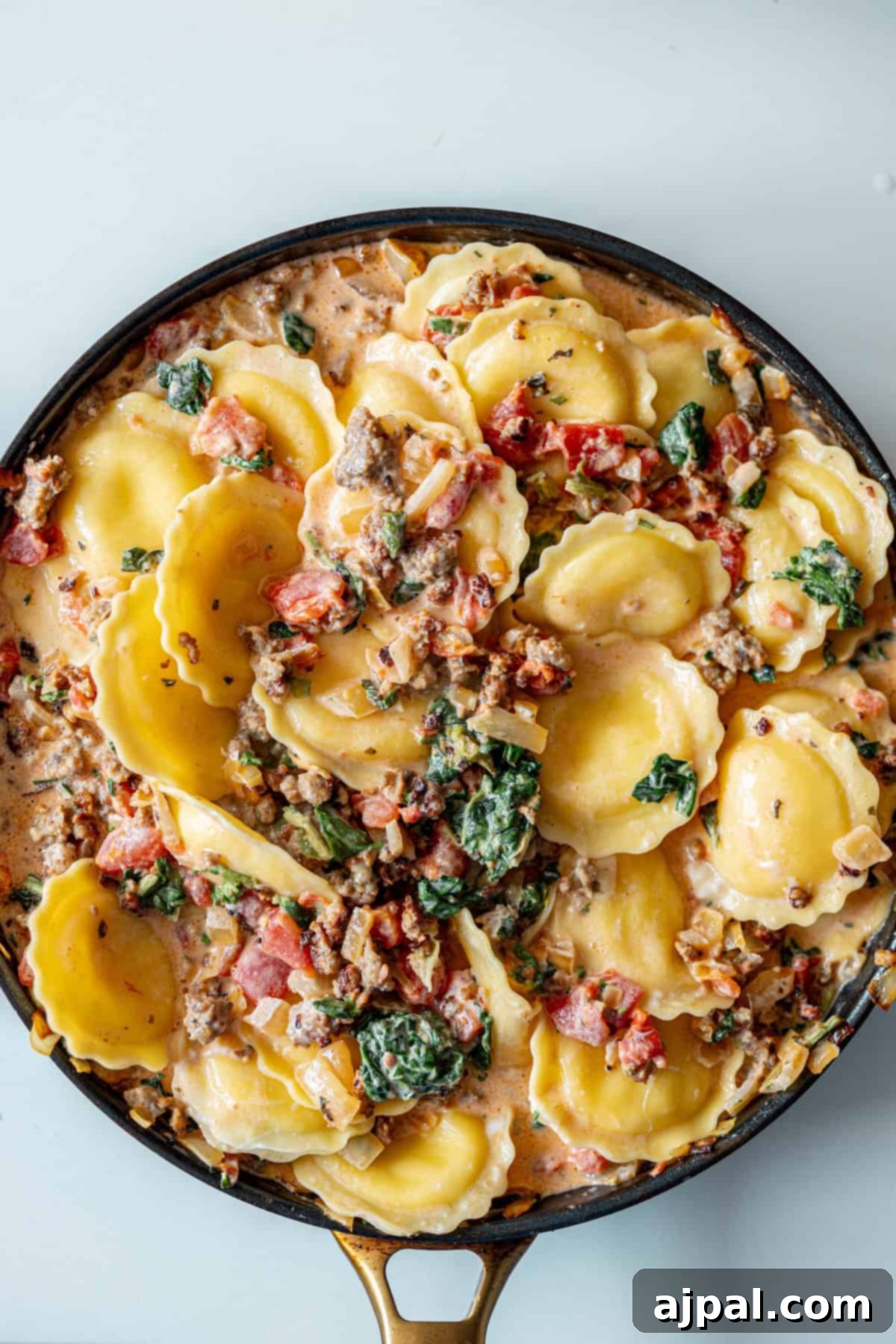 Creamy Tuscan Sausage Ravioli 13 A pan filled with a delicious One Pot Creamy Ravioli and Sausage Skillet—ravioli in a creamy sauce with ground meat, spinach, and diced tomatoes, ready to serve.