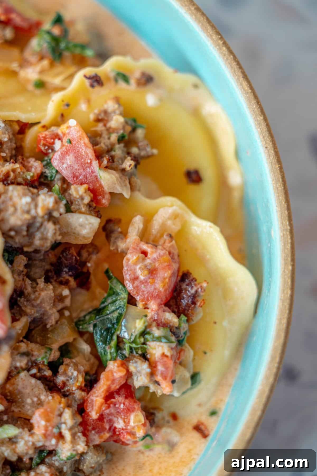 Creamy Tuscan Sausage Ravioli 14 Close-up of a bowl of ravioli pasta, generously topped with a creamy sauce, ground meat, diced tomatoes, fresh spinach, and fragrant herbs—perfect for a satisfying One Pot Creamy Ravioli and Sausage Skillet.