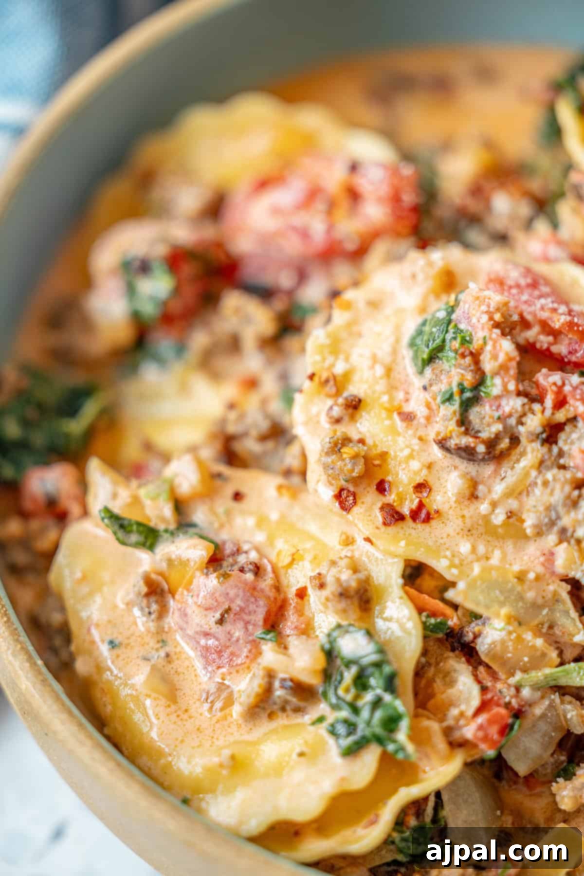 Creamy Tuscan Sausage Ravioli 15 A close-up of a delectable One Pot Creamy Ravioli and Sausage Skillet, showcasing perfectly cooked ravioli, savory ground meat, fresh spinach, and rich tomatoes in a creamy sauce, garnished with herbs in a bowl.
