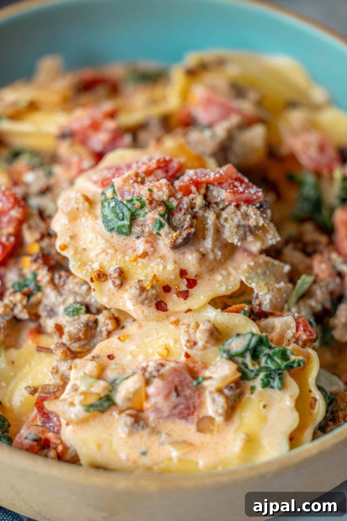 Creamy Tuscan Sausage Ravioli 5 Delicious tomato cream sauce ravioli, topped with ground meat, tender spinach, diced tomatoes, and a rich, velvety sauce in a serving bowl.