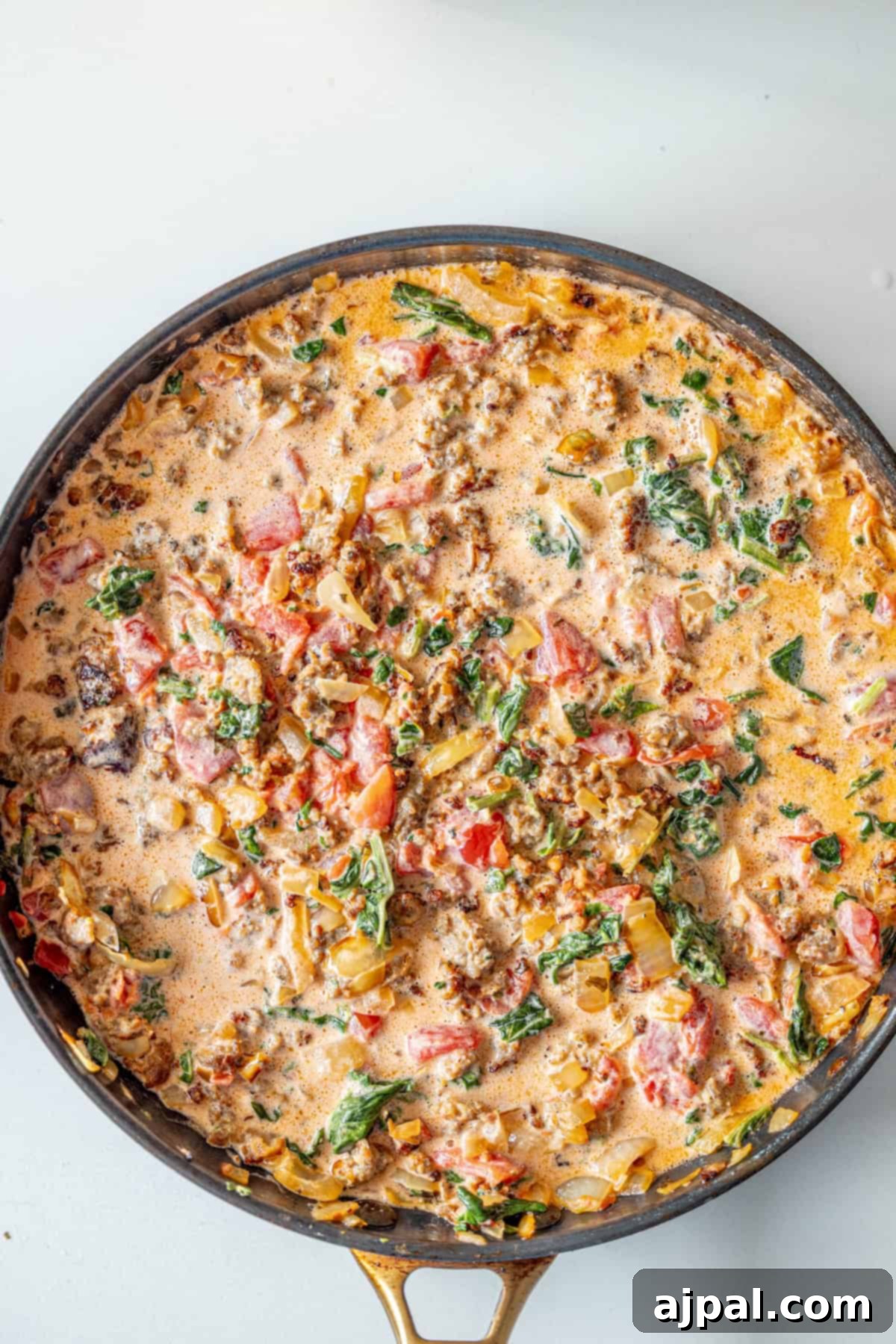 Creamy Tuscan Sausage Ravioli 9 A creamy mixture of ground meat, chopped tomatoes, spinach, onions, and herbs simmering in a skillet, perfect for a hearty ravioli with tomato spinach cream sauce.