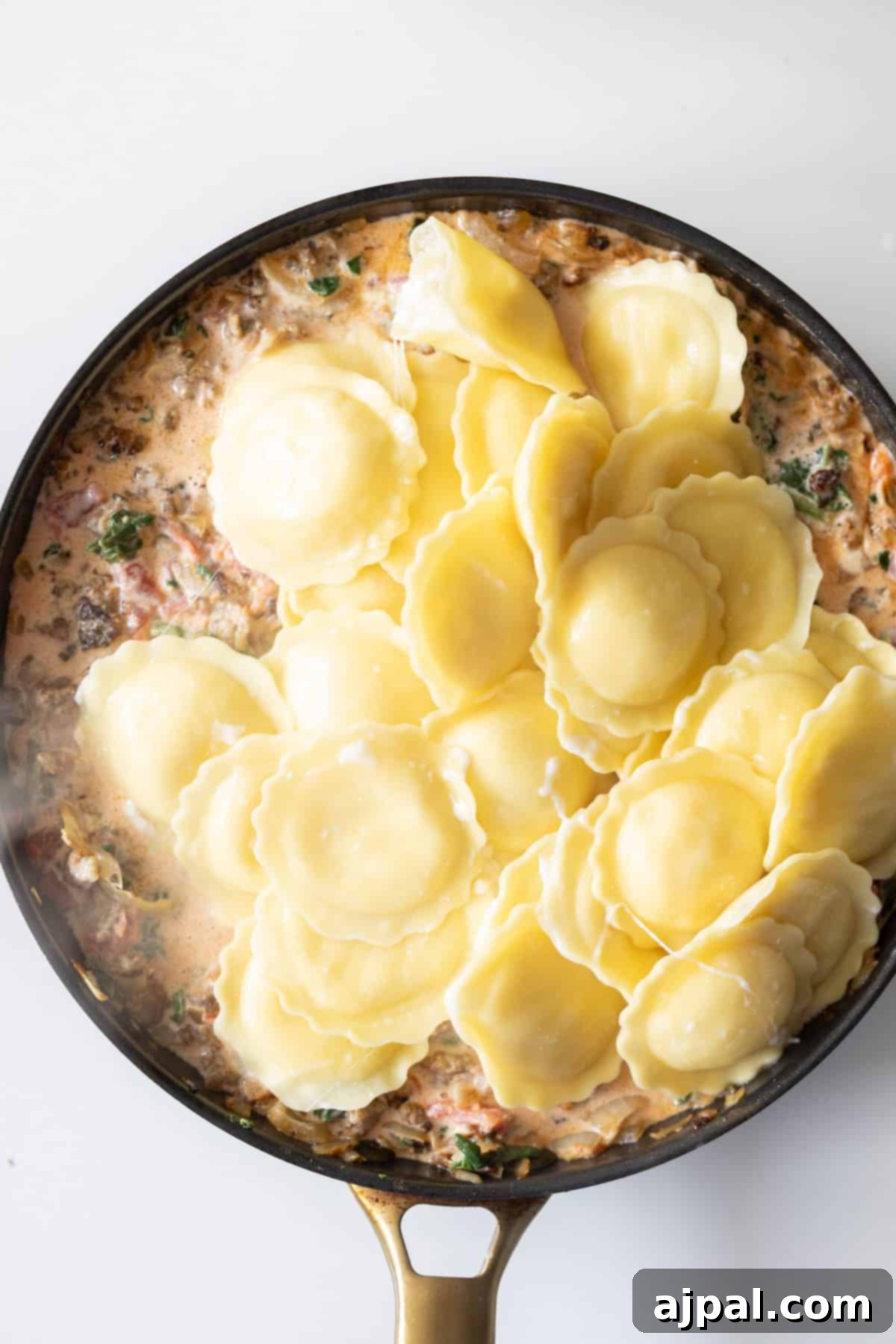 Creamy Tuscan Sausage Ravioli 10 Stuffed ravioli nestled in a creamy spinach tomato sauce with herbs and diced vegetables in a skillet, creating a delicious one-pot meal.