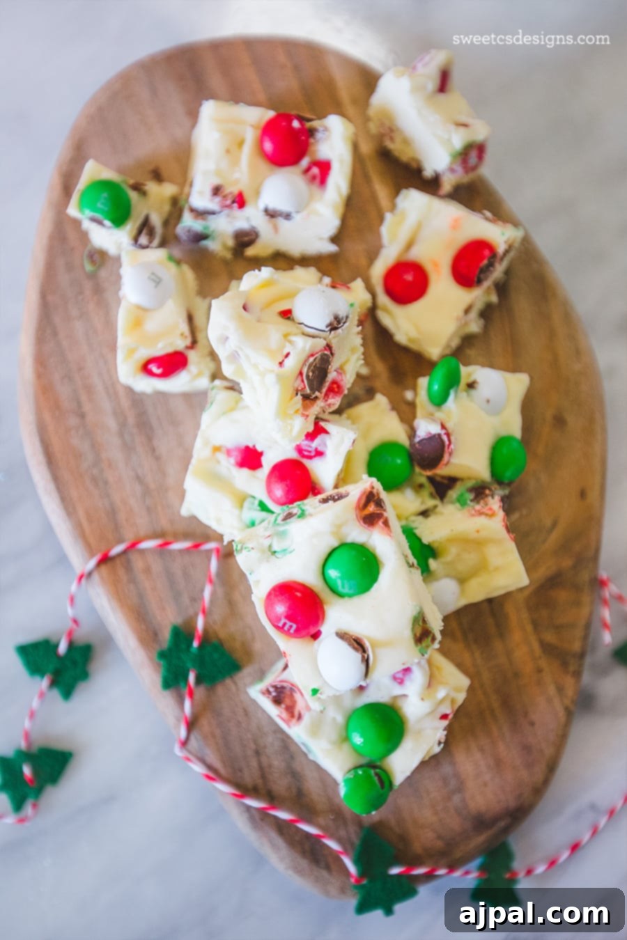Festive Confectionery Fudge 5 Several pieces of rich cookie dough fudge, generously topped with an array of colorful Christmas candies, neatly stacked on a wooden cutting board.