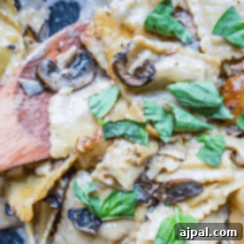 Close-up of creamy mushroom and spinach pasta garnished with fresh basil leaves, mixed and served with a wooden spoon.