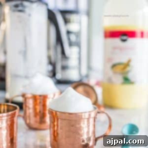Picture of a copper shooter mug with foam on the countertop, garnished with a candy cane.
