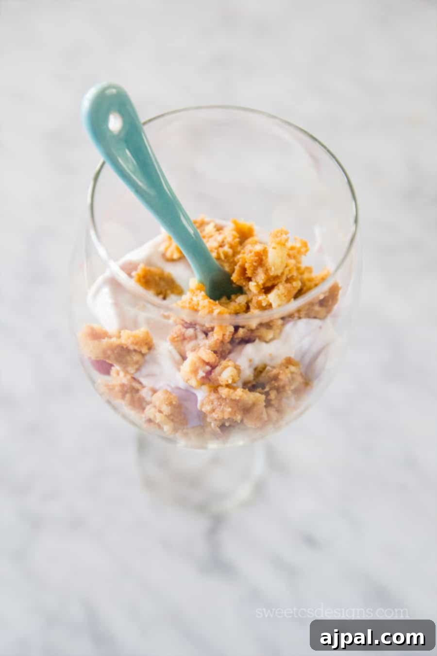Upcycled Pie Parfaits 3 A close-up shot of a gourmet leftover pie parfait served in a sleek wine glass. The layers of creamy yogurt, vibrant pie filling, and golden granola crumbles are clearly visible, topped with fresh berries. A blue spoon hints at immediate enjoyment.