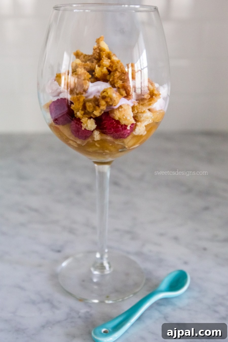 Upcycled Pie Parfaits 4 A beautifully presented leftover pie parfait, layered in a glass. Visible are vibrant red berries, creamy white yogurt, and golden-brown granola clusters, with a blue spoon resting beside the glass, ready for enjoyment.