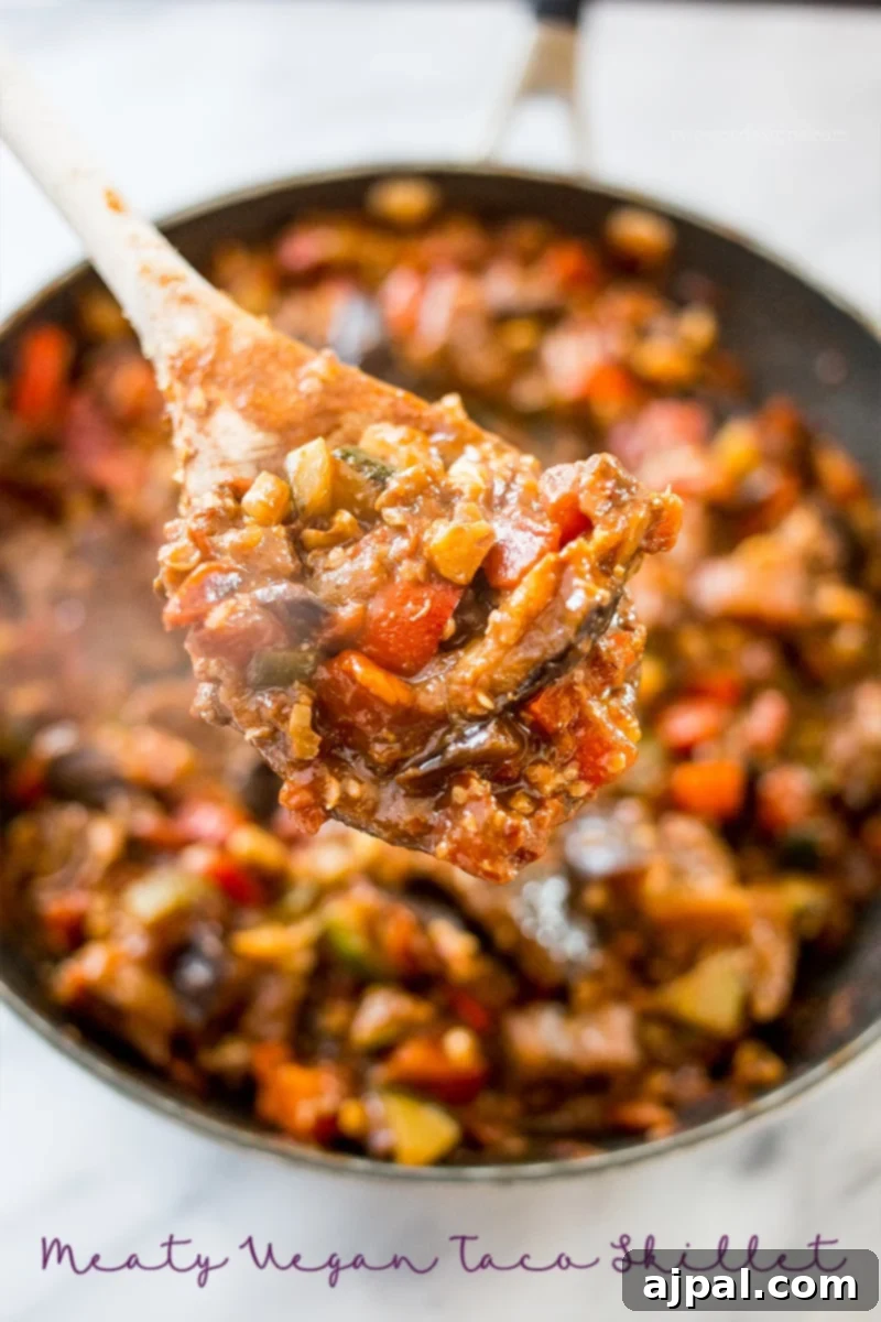 Hearty Paleo Vegan Taco Skillet 4 A wooden spoon stirring a rich, savory vegan taco skillet, highlighting the texture of the vegetables, eggplant, zucchini, and walnuts.