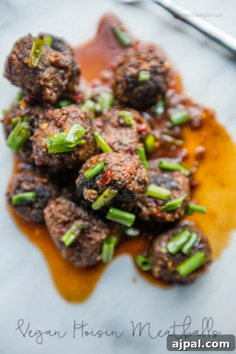 Sticky Vegan Hoisin Meatballs 2 Vegan Hoisin Meatballs served in a pile with rich Asian sauce on top and garnished with fresh green onions.
