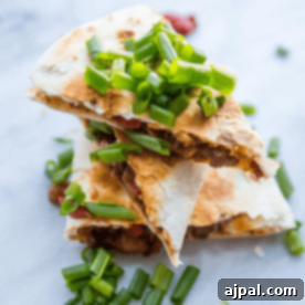 A stack of perfectly cooked meaty vegan quesadillas, garnished with fresh green onions, showcasing the delicious plant-based meal.