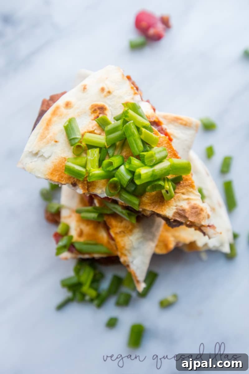 Another mouth-watering view of delicious vegan quesadillas, stacked high with a savory, meaty-tasting filling and garnished with green onions.