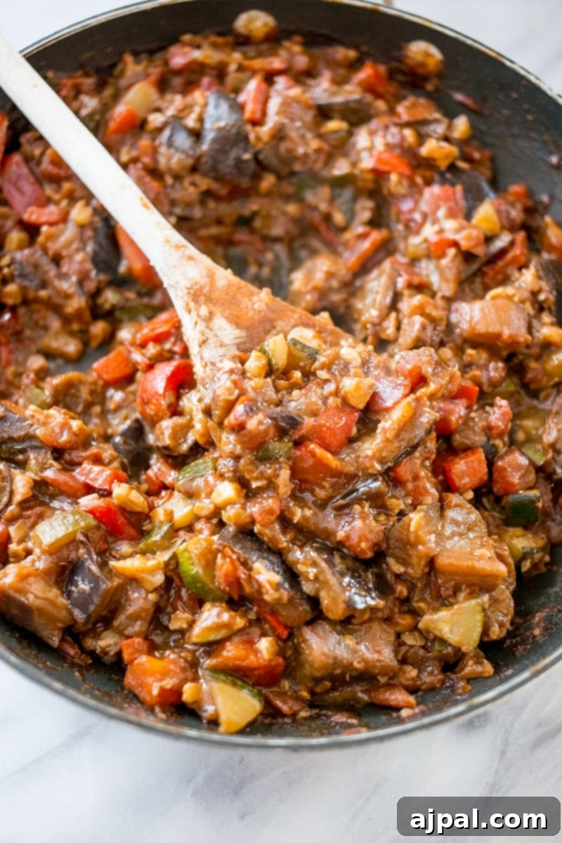 A close-up of a flavorful vegan taco skillet, filled with cooked vegetables like zucchini, bell peppers, and tomatoes, being stirred with a wooden spoon, showcasing the rich texture.