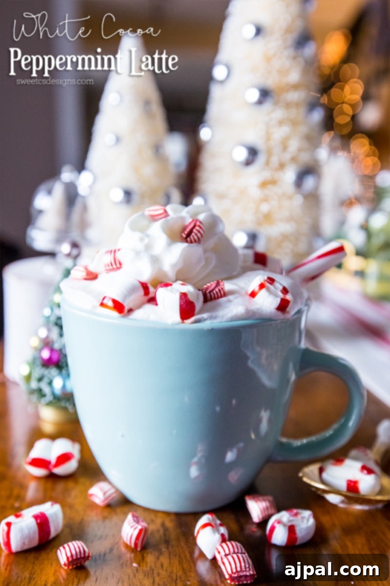 White Peppermint Mocha 4 A festive white cocoa peppermint latte in a mug, topped with whipped cream and garnished with peppermint candies, sitting on a wooden surface amid holiday decor.