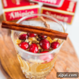 Ginger Mulled White Wine 7 A glass of clear ginger mulled white wine topped with cranberries and a cinnamon stick, set on a wooden surface.