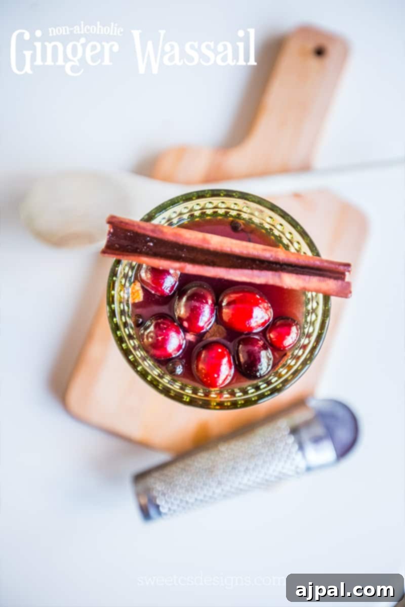 Pink wassail in a green glass with cranberries and cinnamon, placed on a wooden cutting board.