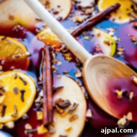 A pot of non-alcoholic ginger wassail, infused with sliced oranges and apples, cinnamon sticks, and cloves, stirred gently with a wooden spoon.