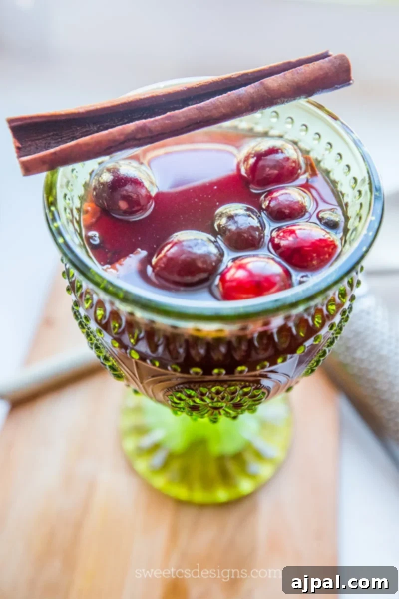 Pink wassail in a green glass with cranberries and cinnamon garnish.