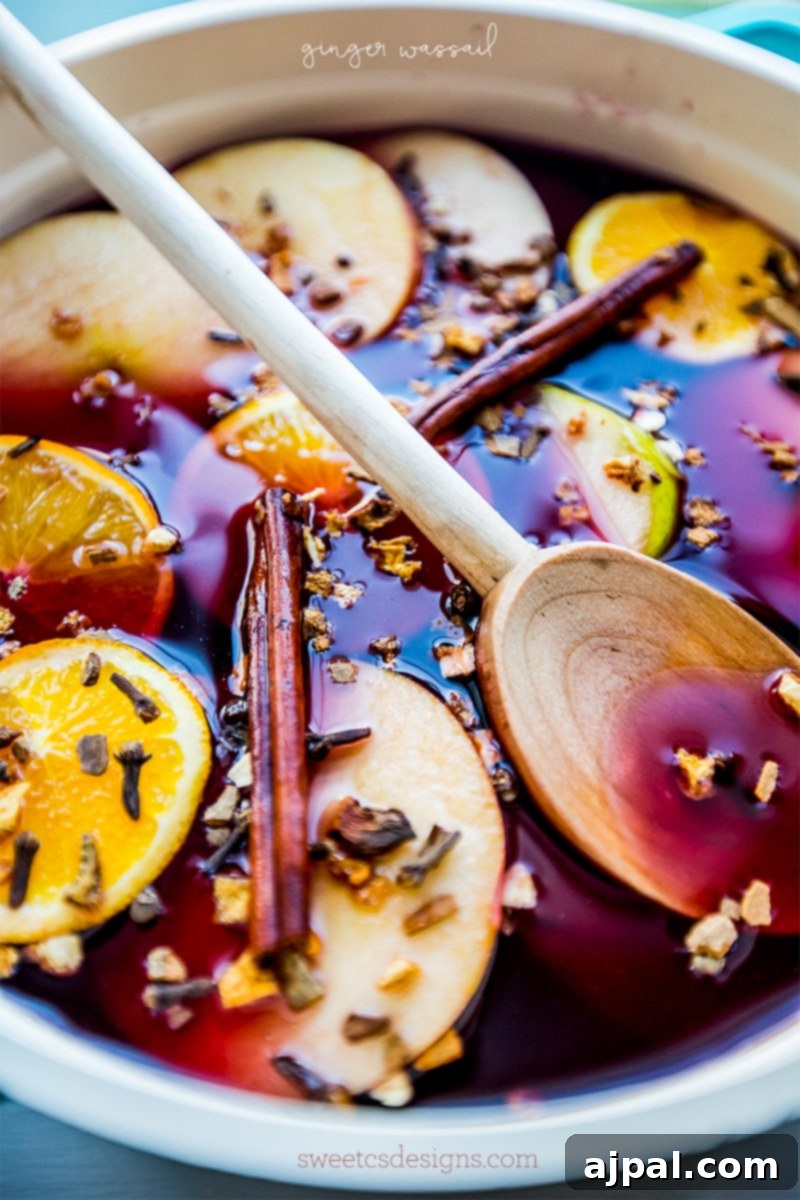 Pink drink with orange slices, apple slices, cloves, and cinnamon sticks, presented in a bowl with a wooden spoon.