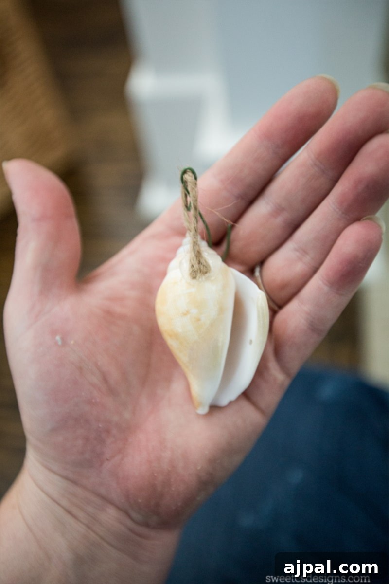 Easy Seashell Tree Decorations for a Coastal Vibe 8 A close-up view of a person crafting easy seashell ornaments for a beach themed Christmas tree, demonstrating how to glue jute loops to the back of seashells for hanging.