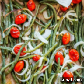 Roasted Green Bean Salad featuring cherry tomatoes and sliced onions, all perfectly arranged on a baking sheet.