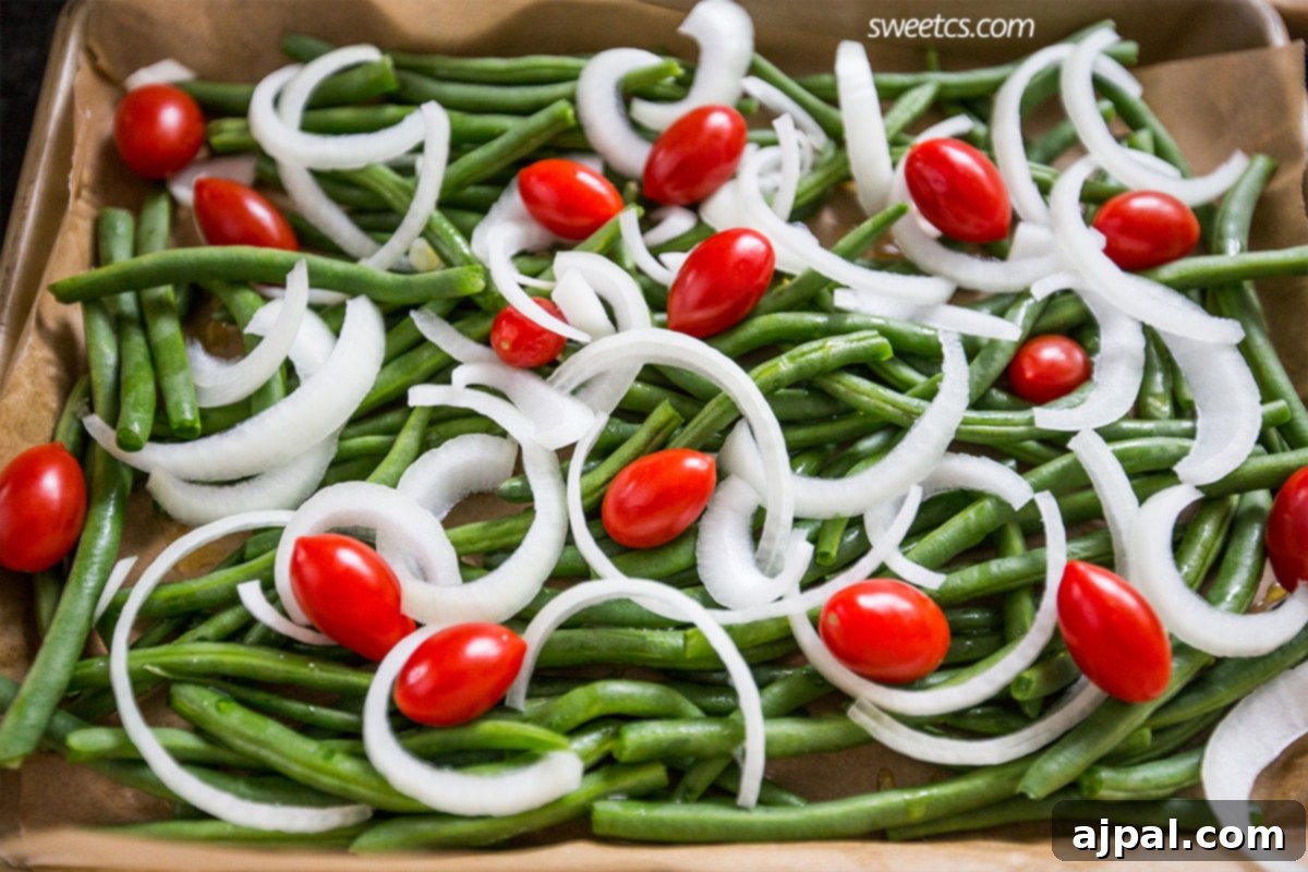 A beautifully roasted green bean salad with tender green beans, caramelized onions, and burst cherry tomatoes on a baking sheet, ready to serve.