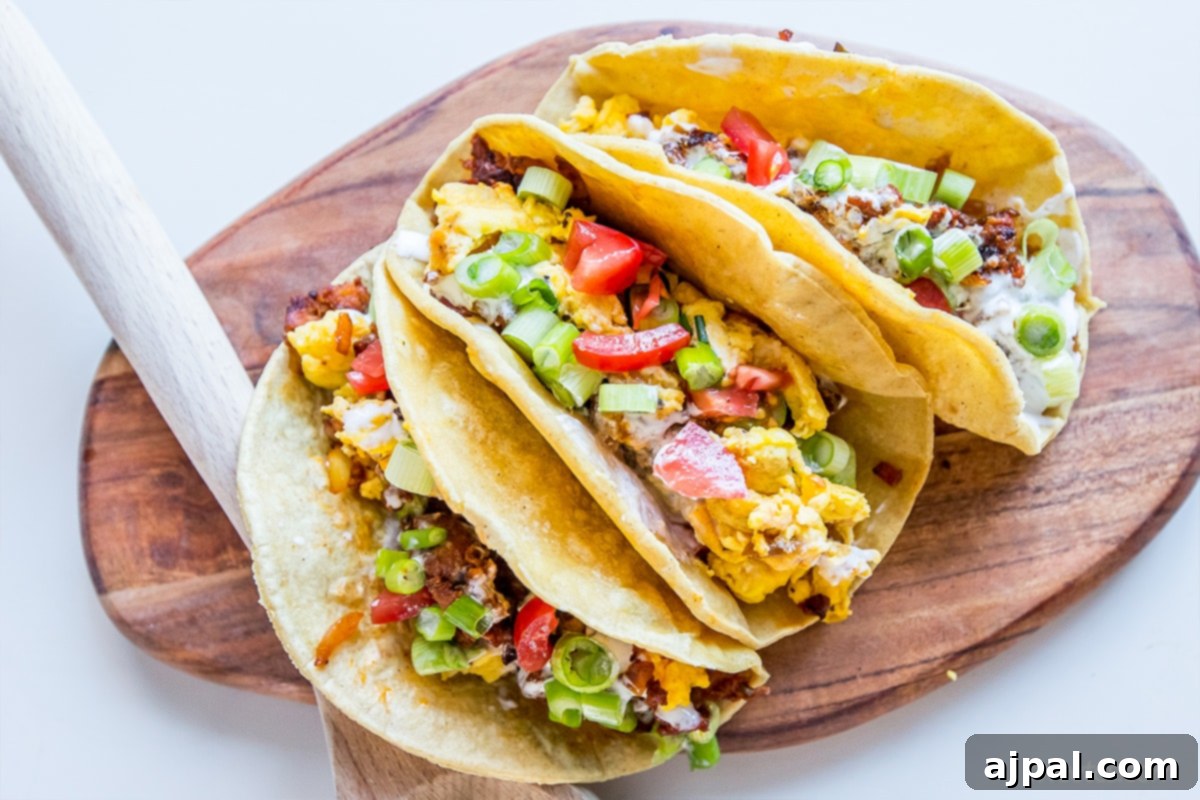 Delicious spicy egg and chorizo breakfast tacos served on a wooden cutting board, garnished with fresh green onions and diced tomatoes. Perfect for a hearty breakfast or brunch.